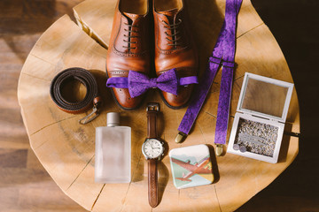 set of groom bow tie, watch, suspenders, belt and perfume lie on the background of vintage wooden table