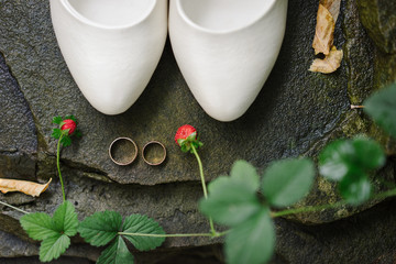 wedding rings, white leather bride's shoes and growing strawberries on stone background