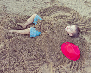 Cute kid burried in the sand for fun