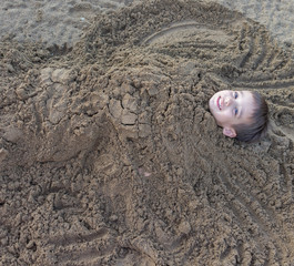 Cute kid burried in the sand for fun