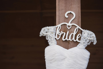 closeup of white wedding dress on custom wooden hanger on wooden background