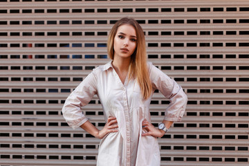 Fashionable pretty woman in a summer dress posing near a metal grid wall