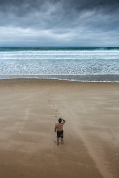 Lonely man staring at overcast beach. 

Loneliness is a complex emotion who response to isolation. Overcast is the meteorological condition of clouds obscuring all of the sky. 