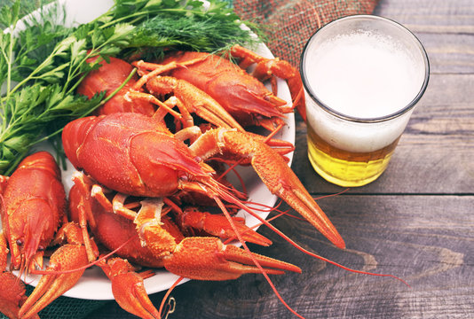 Glass of beer and a boiled crawfishes in a plate on a wooden background, top view