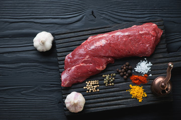 Raw fresh machete beefsteak, black wooden background, above view