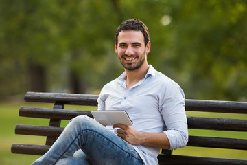 Obraz premium Young businessman is sitting at the park and using digital tablet.