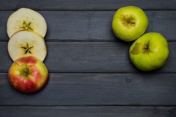 Whole and cut red and green ripe apples autumn harvest and apple juice, from above on dark grey wooden table