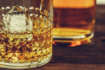 glass of whiskey with ice cubes near bottle on wood table, warm atmosphere