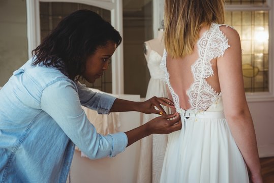 Woman trying on wedding dress with the assistance of fashion des
