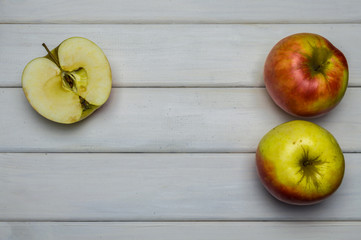 Whole and cut red and green ripe apples autumn harvest, from above on white wooden table