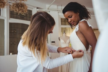Woman trying on wedding dress with the assistance of fashion des