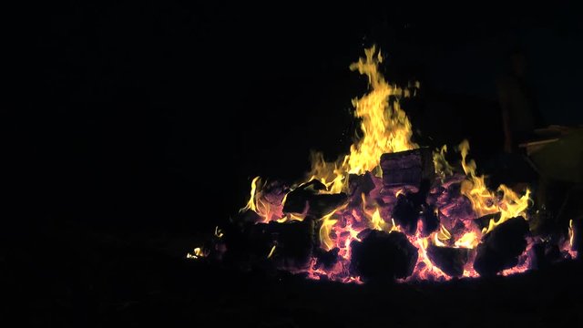 Someone adds firewoods to a huge bonfire, closeup shot