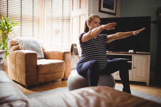 Pregnant woman performing stretching exercise on fitness ball in