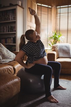 Pregnant woman performing stretching exercise on fitness ball in