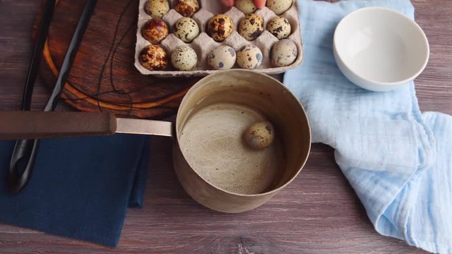 Putting fresh quail eggs into small scoop for cooking or quality control. Kitchen interior with wooden table, cardboard packing, bowl, dipper and napkins, tissue.