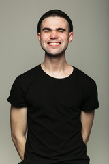 Obraz premium Portrait of young stylish toothy smiling man with closed wink eyes on gray background in studio.