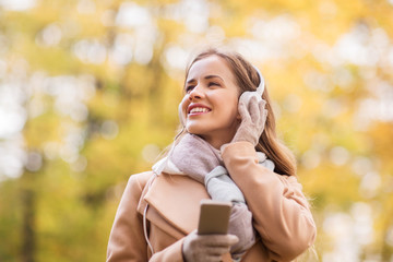 woman with smartphone and earphones in autumn park