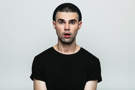 Isolated portrait of emotional shocked man wearing black t-shirt and hat with opened mouth. Front view. Studio shot on gray background.