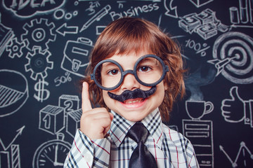 Little boy as businessman or teacher with mustache and glasses standing on dark background pattern. Wearing shirt, tie. Lifting a finger up