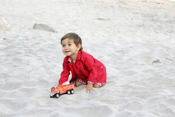 baby playing with a firetruck in a beach
