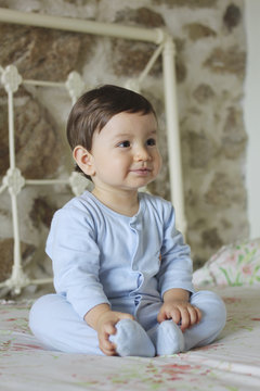 smiling baby sitting in bed with stone background