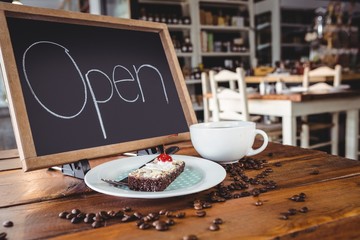 Open signboard with slice of cake and coffee cup on a table