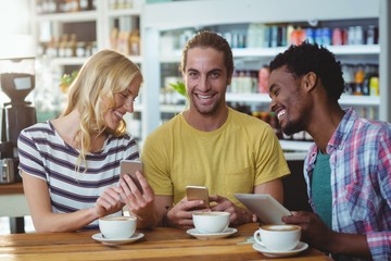 Three friends using mobile phones while having cup of coffee