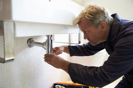 Plumber Working On Sink In Bathroom