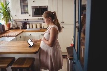 Pregnant woman using digital tablet in kitchen
