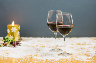 Christmas cheers with two glasses of red wine on snow with a golden candle flame