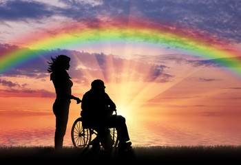 Silhouette of nurse caring for a disabled person in a wheelchair on a rainbow background