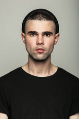 Obraz premium Headshot of young stylish man in black T-shirt and hat standing in studio on grey background. 