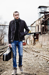Young musician with guitar case is going among industrial ruins