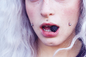 Primer plano de la boca de una chica joven con piercings comiendo una mora 
