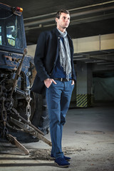 Fashion shot: handsome young man wearing jeans and coat against the tractor