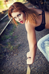 Beautiful redhead girl in bra and jeans pulls a railway lever. Closeup