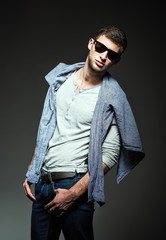 Fototapeta premium Studio fashion shot: handsome young man wearing jeans, shirt and sunglasses