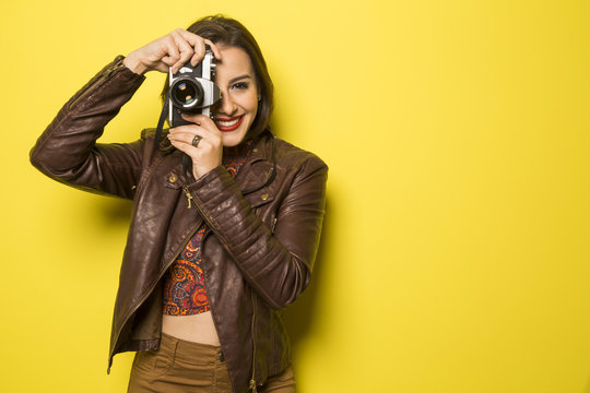 Fashion young girl makes the photo with old camera. Yellow backg