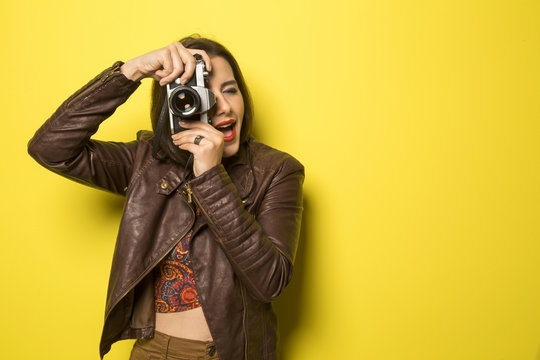 Fashion young girl makes the photo with old camera. Yellow backg