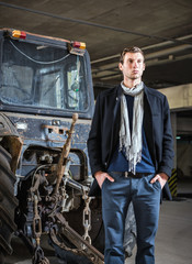 Fototapeta na wymiar Fashion shot: handsome young man wearing jeans and coat against the tractor