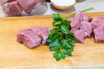 Raw pork neck meat cut in slices and fresh parsley on wooden cutting board