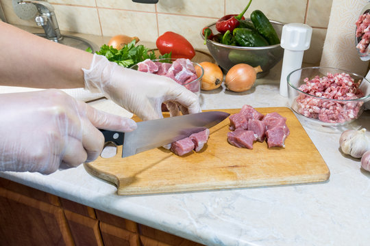 Woman is cutting fresh pork on a wooden cutting board in the modern kitchen surrounded by fresh food .