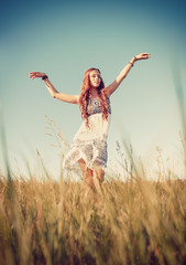 Beautiful young hippie girl dancing in the field at sunset time
