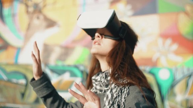 Brunette woman uses 3D Virtual Reality headset on bright background outdoors 4k