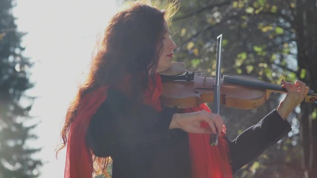 Violinist begins to play. Woman violinist in the forest. A musician with a bright appearance: red hair, red scarf. Violin, bow. Classical music. Green trees. Philosophy. Marvelous