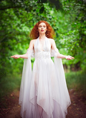 Obraz na płótnie Canvas Beautiful redhead woman in white dress among trees