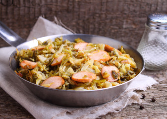 Cabbage stew with sausages in a frying pan on a wooden background