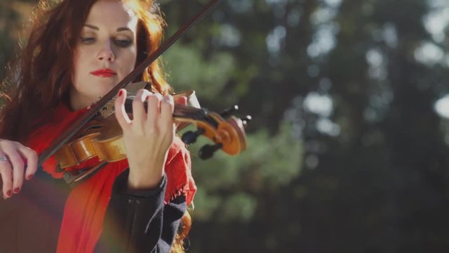 Woman flames. Passion. Passionate woman musician playing the violin. Professional musician playing in the woods. Violinist with red hair and red lips. Talent. Perseverance.