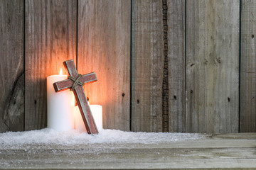 White candles glowing behind wood cross