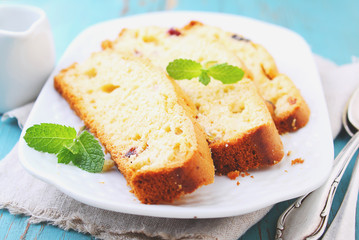 a piece of cake with raisins and candied fruit on a white plate on a blue background